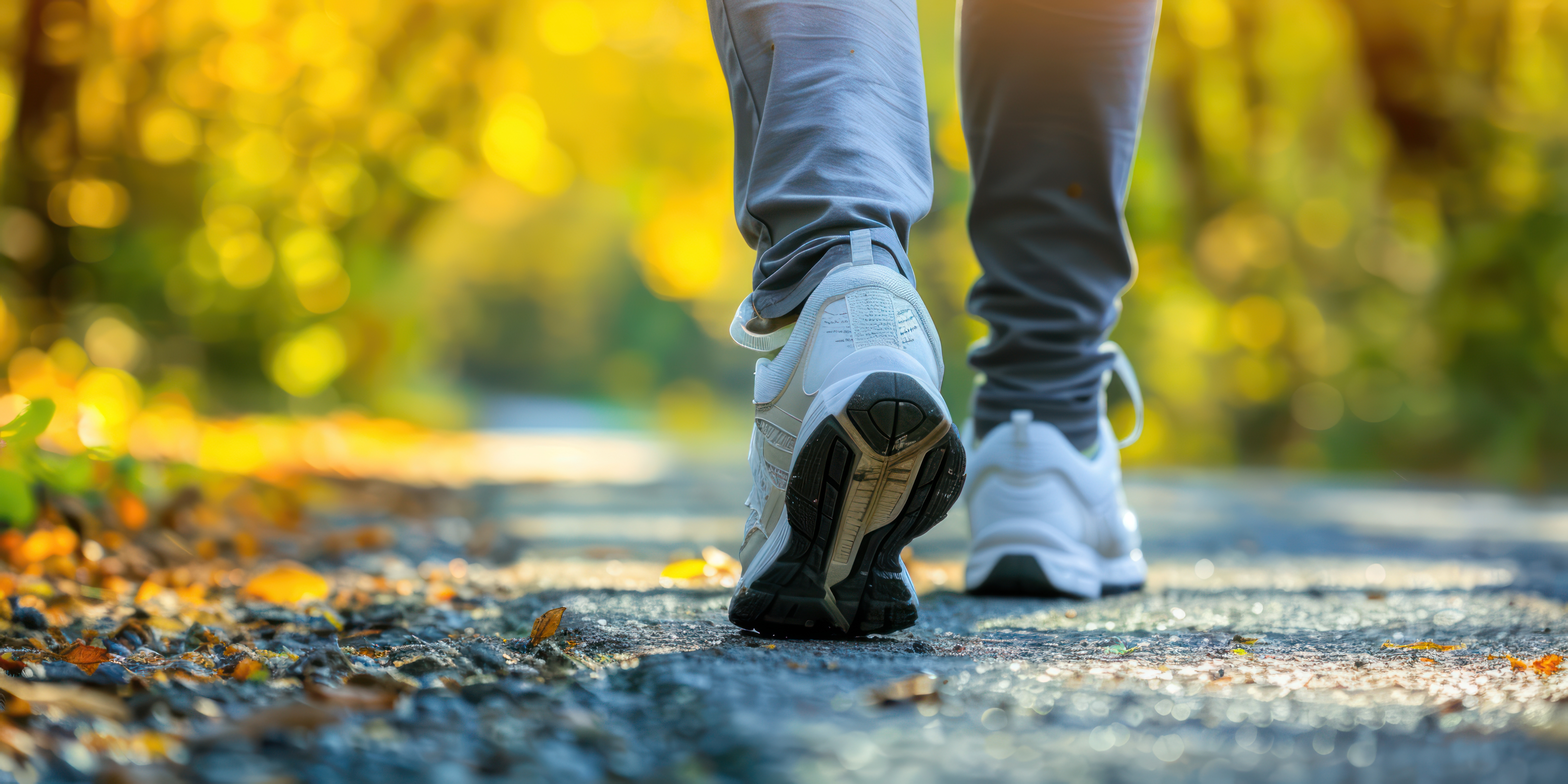 Ground shot of person in white tennis shoes and gray pants hiking on gravel through a forest.