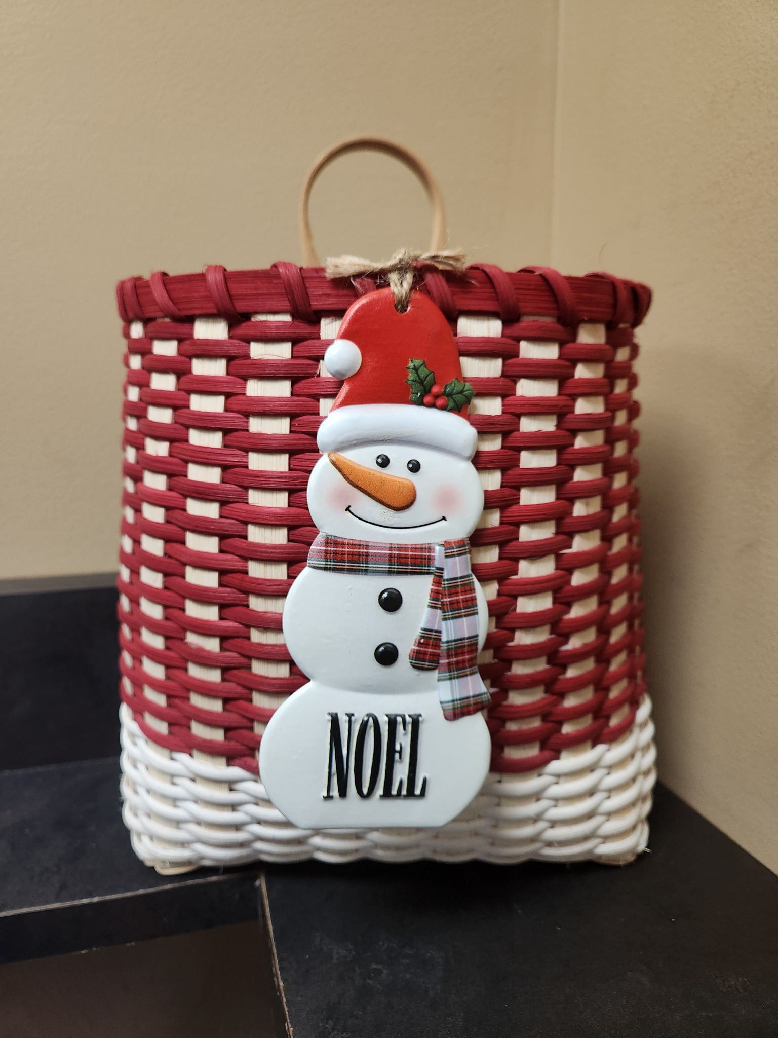 A Red and White Christmas basket with a snowman on the front and the word NOEL on the bottom of the snowman.