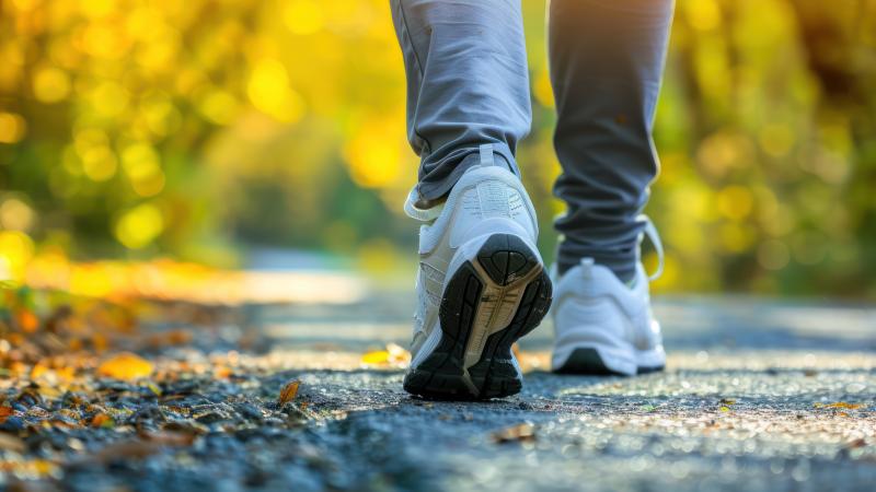 Ground shot of person in white tennis shoes and gray pants hiking on gravel through a forest.