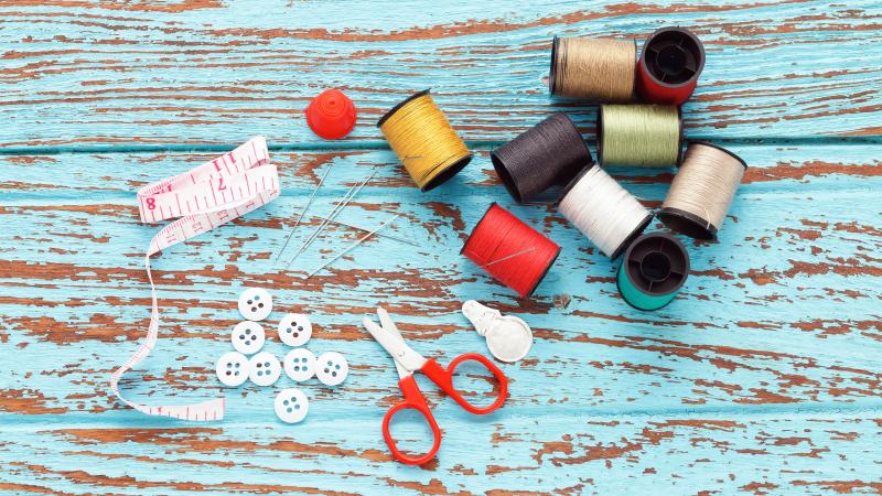 Sewing thread, scissors, measure, and buttons on a wooden blue table